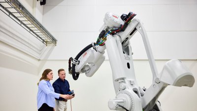 Dva inženýři programující velké, bílé průmyslové robotické rameno ABB v laboratorním prostředí.