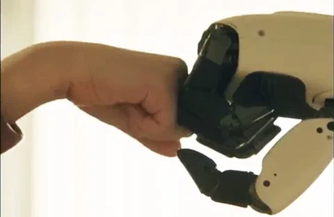 Primer plano de la mano del robot LG CLOiD chocando el puño con una mano humana, simbolizando la interacción hombre-máquina.