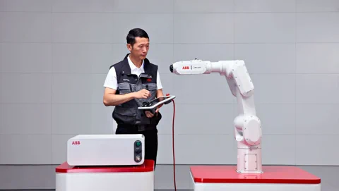 An engineer programming an ABB IRB 1200 robot arm with a tablet controller.